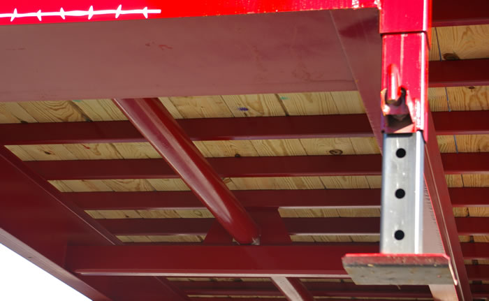 This is a view of the bottom side of a Red Rhino flatbed gooseneck trailer.  Notice the 4 ½”OD pipe running down the center of the frame.  This is the torsion tube.  It is tied to the main-beam at three points.  Also note the underside of Red Rhino hay trailers are primed and painted.  Many trailer manufacturers do not paint the underside.